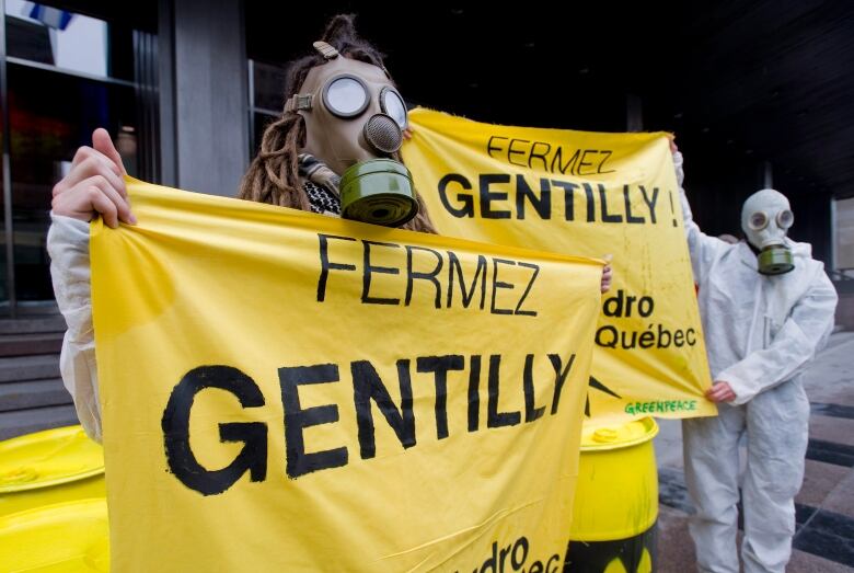 People wearing gas masks and holding up a sign in French that reads, 