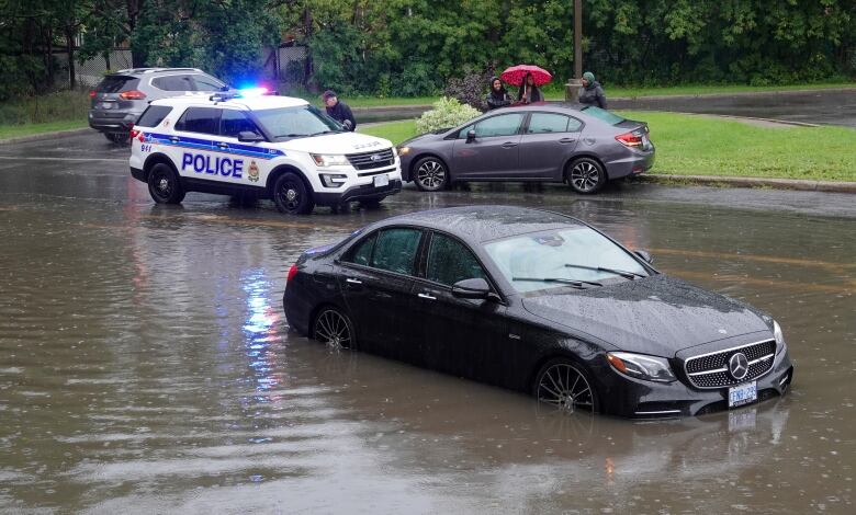 A car is partially submerged in floodwater on a street in Ottawa during a rainstorm