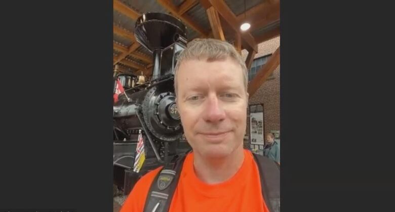 A selfie of a man with an orange T-shirt standing in front of a train in a museum.