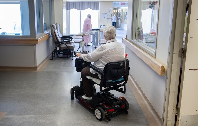 A woman in a long-term care home rides a mobility scooter.