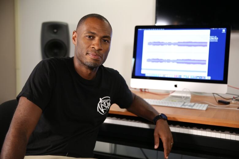 A man poses in front of a computer, with his arm against the desk. 