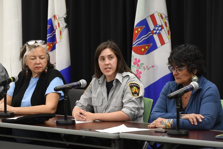 Three woman sit a table behind microphones while the woman in the centre in speaking.