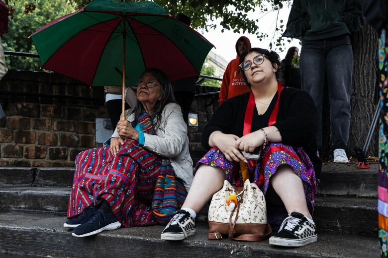 Two people sit on steps. One hold an umbrella.