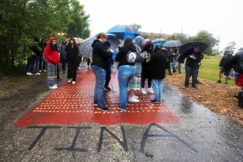 People stand under umbrellas on a paved walkway that says 