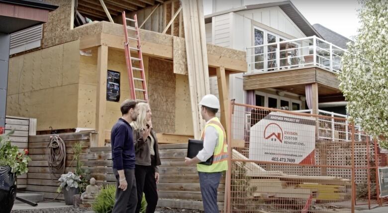 Three people stand outside a house under construction.