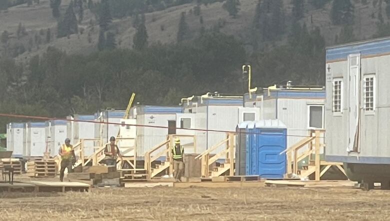 Men in yellow work vests work near container-type modular housing units.