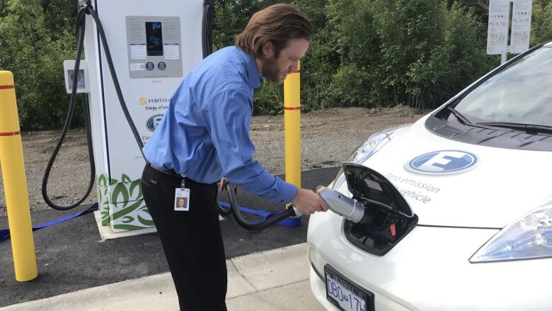 A man connects an electric vehicle charger to a car.