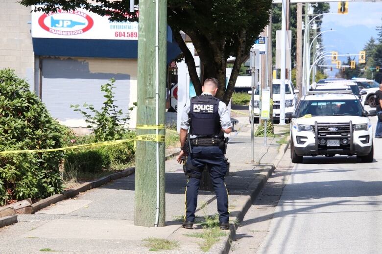 A police officer stands next to a bus stop with police tape closing it off.