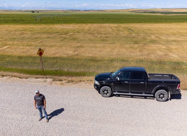 An aerial shot of a man and his truck standing in front of a wheat field. 