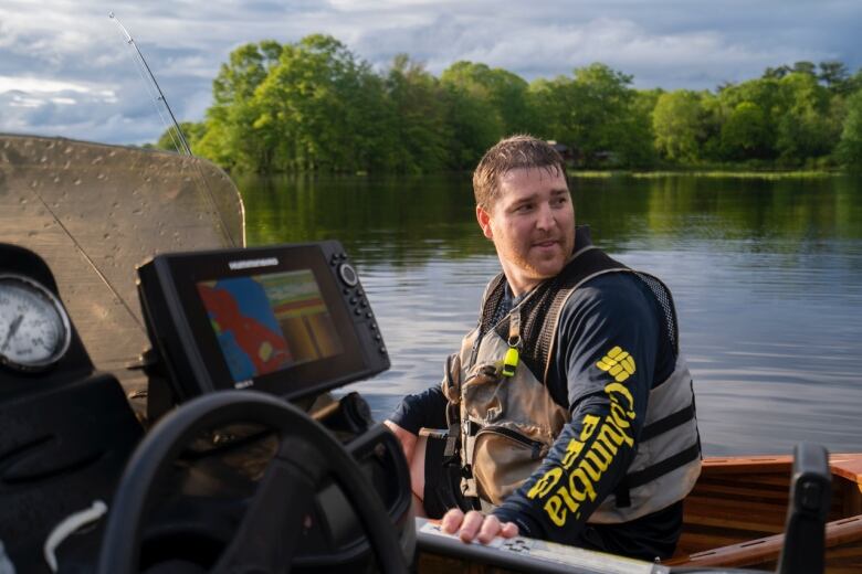 A man in a lifejacket sits in a boat on the river.