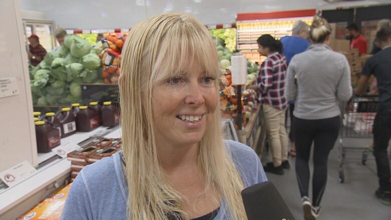 A blonde woman smiles as she talks about saving money at a local grocery store. 