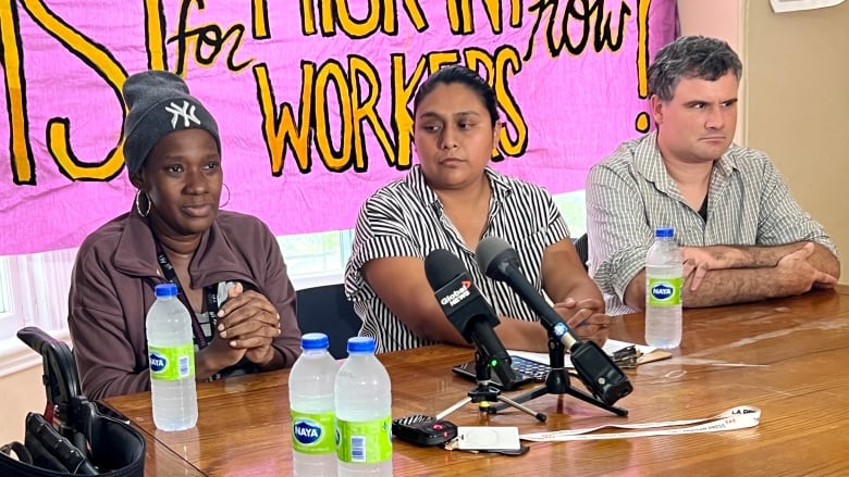 three people sit at a desk with  microphones on top.