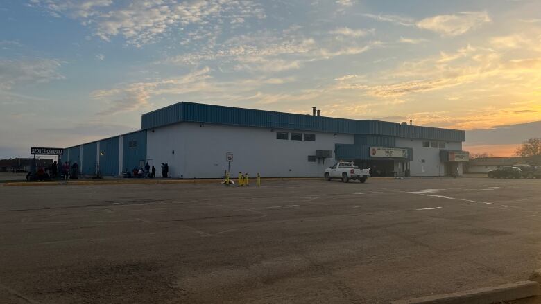 An arena exterior at sunset. There are shadows of people by the building.  