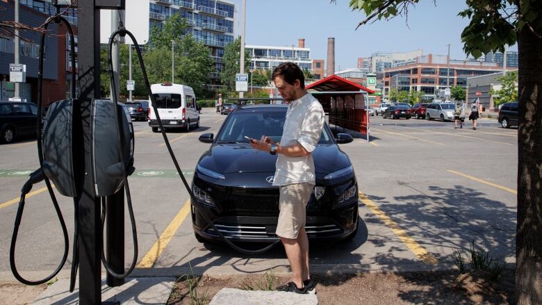 A man checks his phone as he stands in front of a vehicle. 