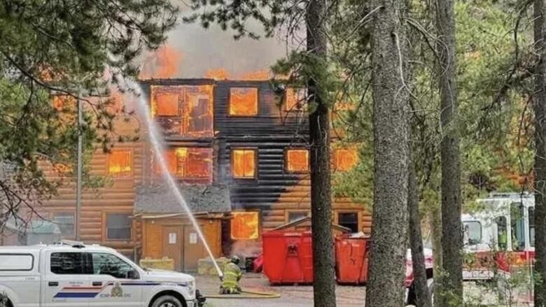 A log building is on fire with an RCMP truck parked in front of it.