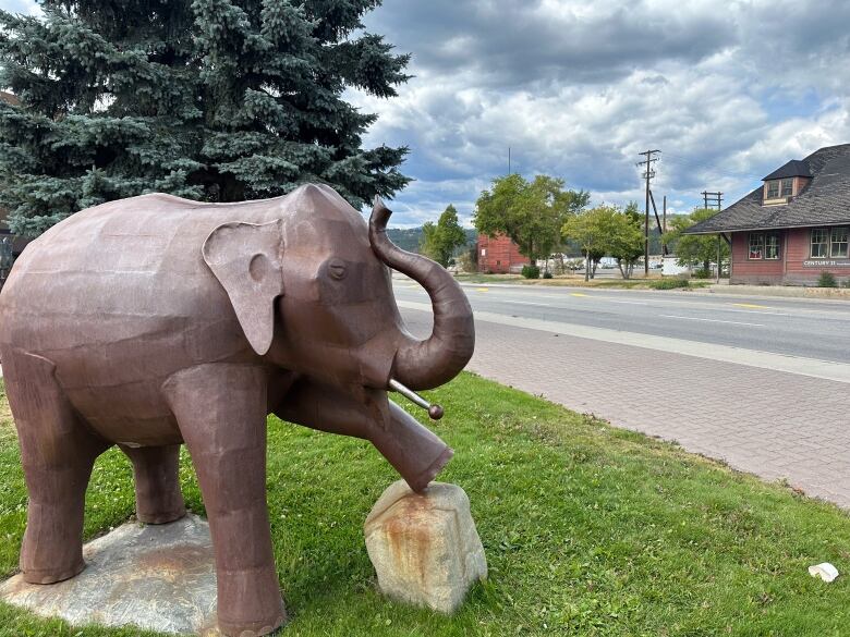 A metal elephant statue with its hoof raised on a small stone block.