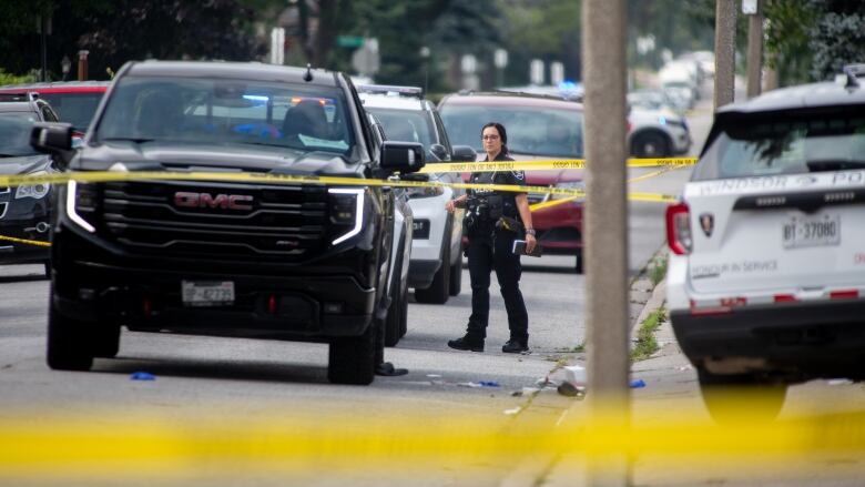 Yellow tape blocks off a street. A police officer stands next to a police vehicle.