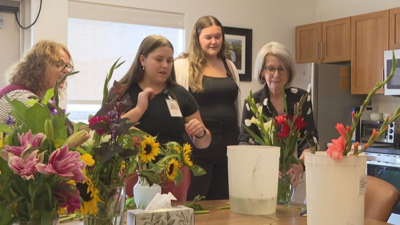 A group of women looking at some flowers set up on buckets lying on a table.