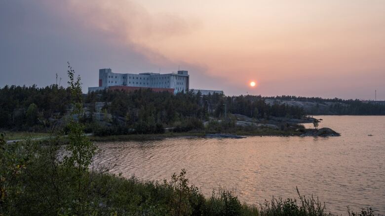 Smokey sky from nearby wildfire over a hospital adjacent to a lake in Yellowknife.