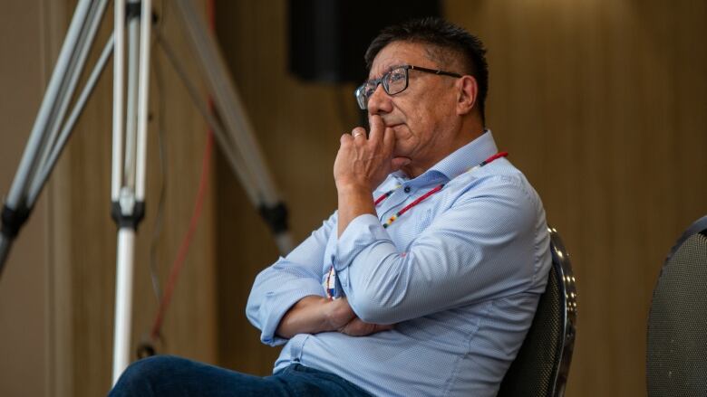 A man sits in a chair listening to someone else speak out of the frame. 