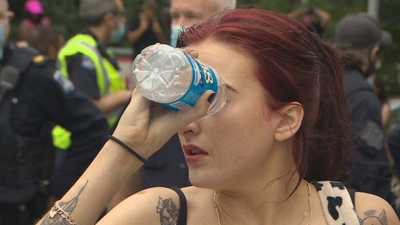 A woman pours water on her eyes from a plastic water bottle to get relief from pepper spray after police used it during a protest in Halifax on August 18, 2021. 