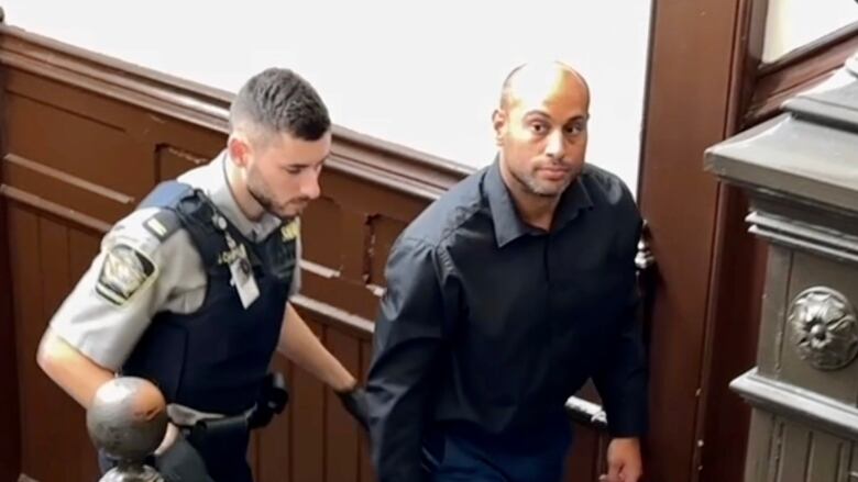 A police officer walks up the stairs behind a man wearing a jacket and jeans.