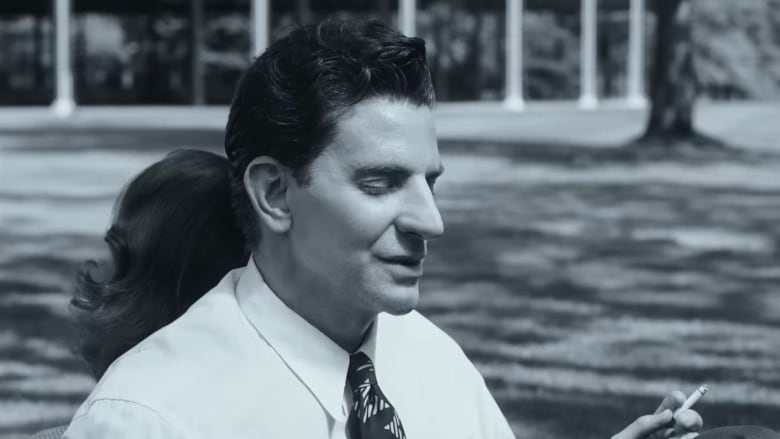 A man with a long nose wears a tie and white dress shirt and holds a cigarette.