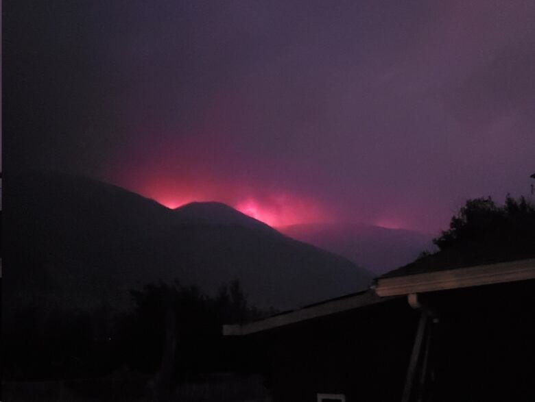 A plume of smoke purple of colour is rising from a mountain in the dark.