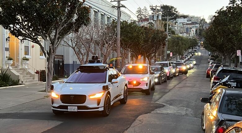 A long line of cars on a San Francisco street, with a white driverless taxi at the front.