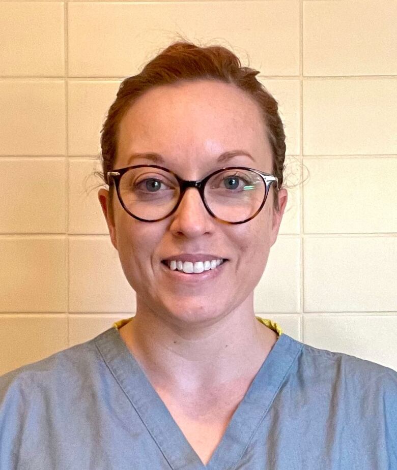 A woman wearing grey scrubs and glasses with her dark hair pulled back.