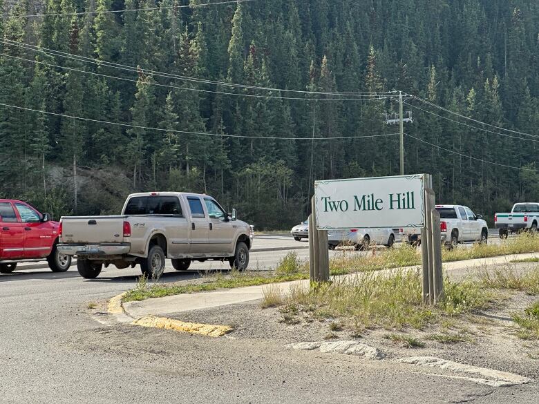 A road with a white sign and cars passing by.