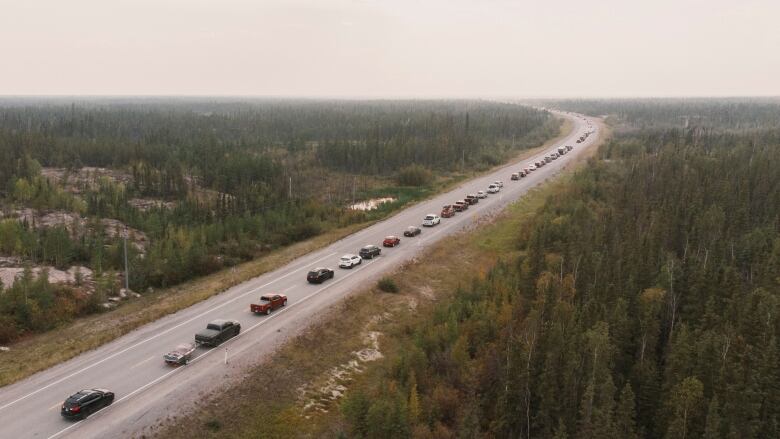 A long line of cars is seen driving in one direction on a rural highway.