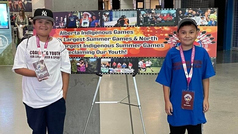 Two boys stand next to a sign announcing the Alberta Indigenous Games.