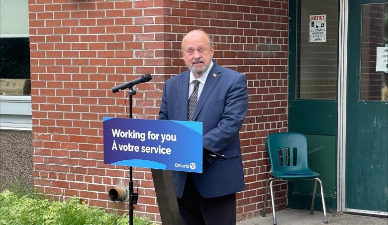 A man stands behind a microphone outside a brick building.