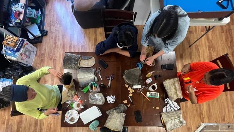 A table is crowded with craft supplies and sealskin. 