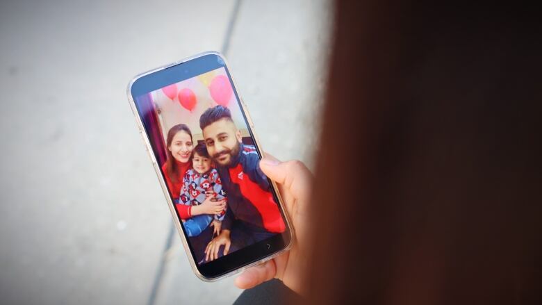 A woman is looking at her phone that shows the photo of a man, woman, and a child. 