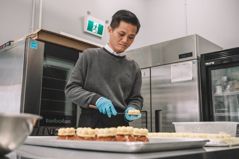 A man working in a commercial kitchen assembles the layers of a choux pastry.