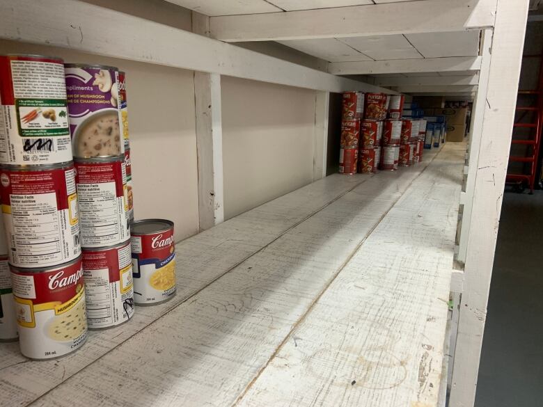 A largely empty white shelf, with some stacks of canned soup.