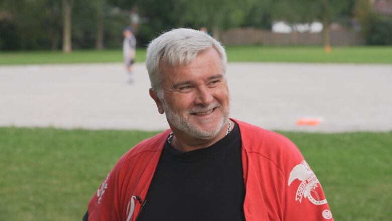 A man in a baseball jersey looks off the screen and smiles.