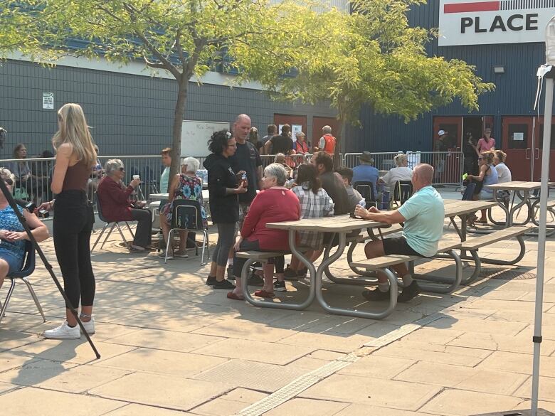 People sit at a picnic table outside an arena that has been turned into an emergency reception centre.