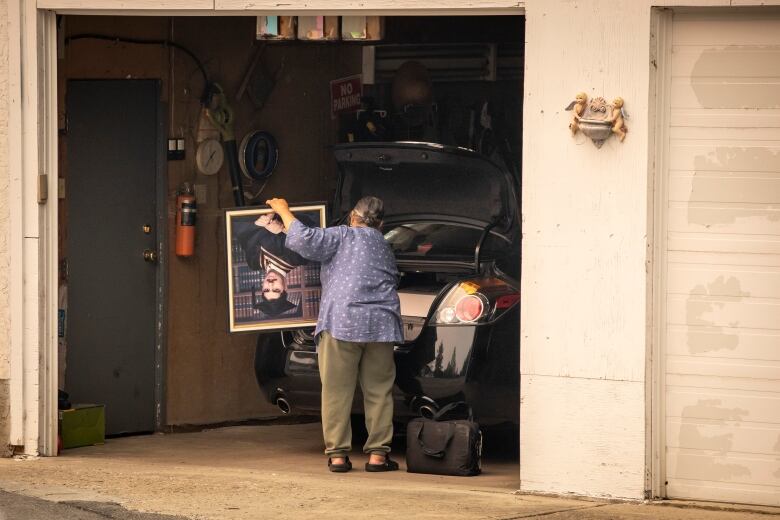 A woman with her back to the camera is packing belongings into a black sedan.