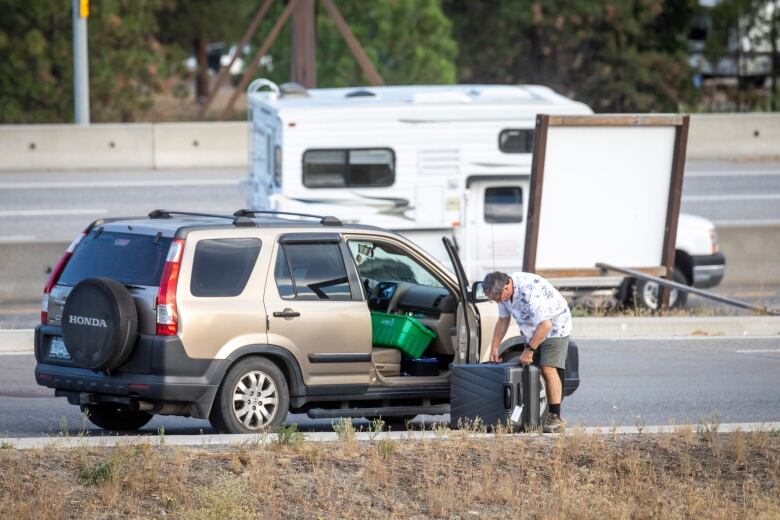 A man packs a suitcase on the side of the highway.