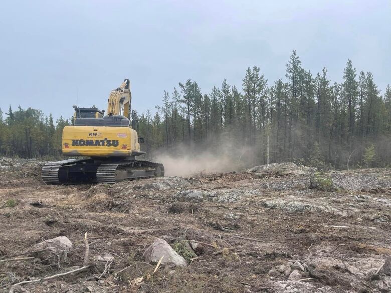 A piece of heavy construction machinery works in a rocky area cleared of trees.