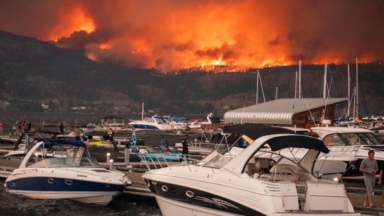 Boats on a lake are pictured against wildfires in the mountain across.