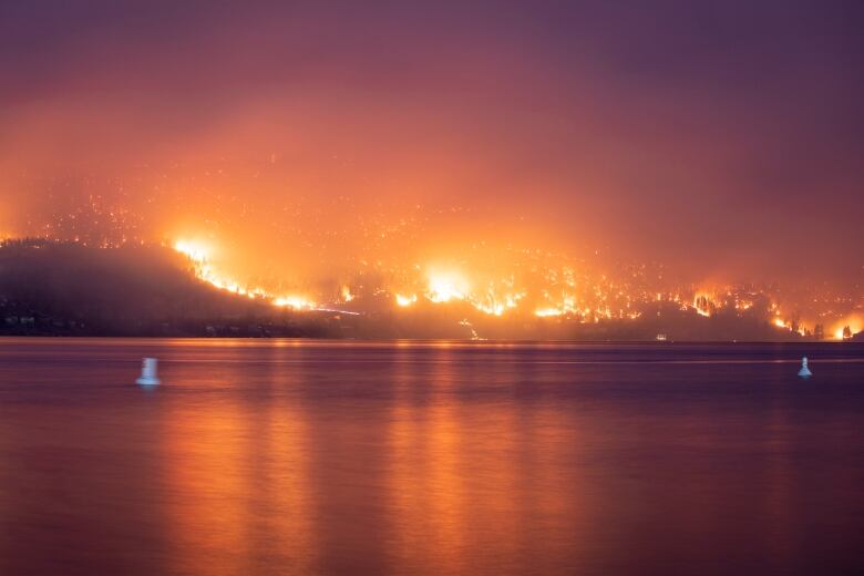 A large wildfire reflects across a pristine lake.