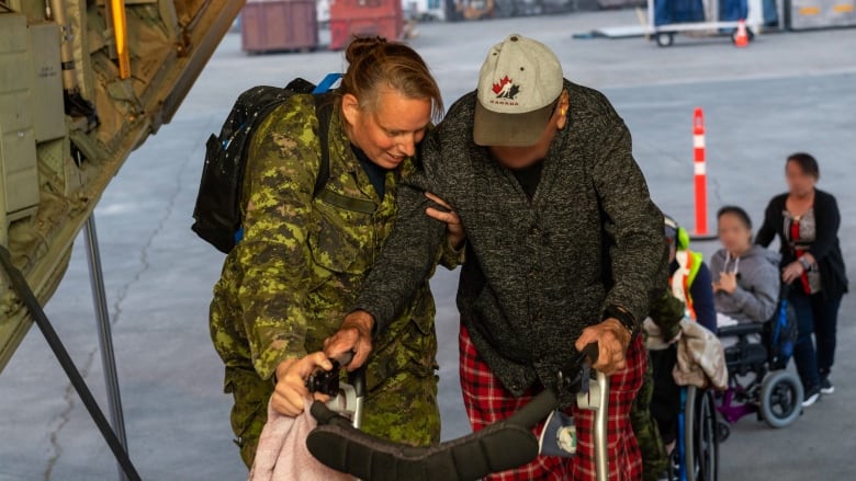 A woman dressed in camouflage helps a man through the loading door of a cargo plane.