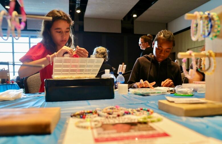 Angel and Olugo sit at a table handling the jewelry they made. 