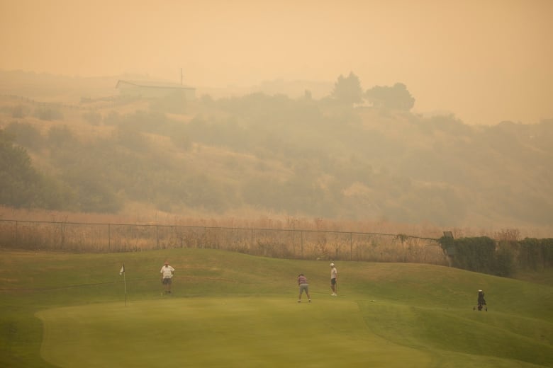 A small number of golfers are pictured amid heavy wildfire smoke.