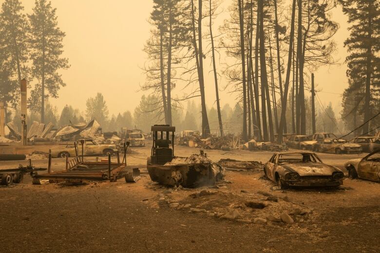 A parking lot full of destroyed vehicles, with wildfire smoke in the air.