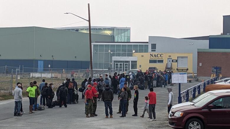 People line up with their luggage in a parking lot outside the Northern Arts and Cultural Centre in Yellowknife. 